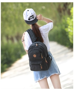 Outdoor view of a black canvas backpack featuring premium leather pullers and multi-zipper layers