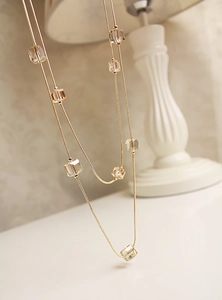 Detalle de collar de doble cadena dorada con cuentas de cristal facetadas