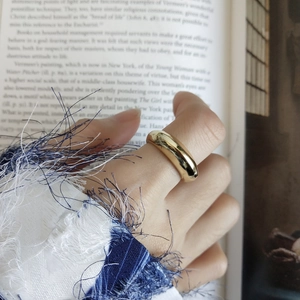 Detailed view of wide gold polished ring worn by a model in a cozy, elegant setting