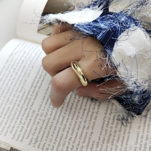 Detail of a minimalist gold ring worn by a model over an open book and blue fabric