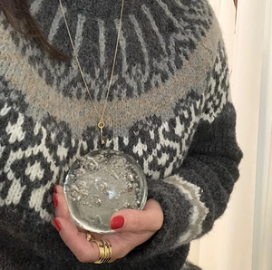 Detailed view of a gold key necklace with bubble glass pendant on a knit sweater