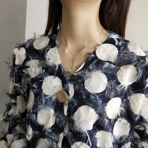 Close-up of golden key pendant necklace and round hammered brooch on a model's outfit
