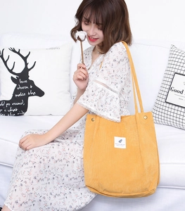 Detail of a large yellow corduroy tote bag with feather patch on a white sofa