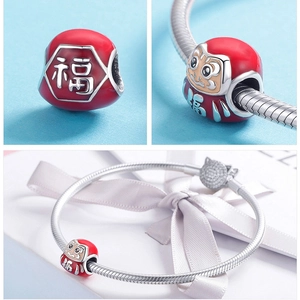 Macro shot of red Daruma fortune charm with Fu character on silver snake chain bracelet