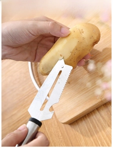 Detail of stainless steel peeler blade removing skin from potato on a wooden board