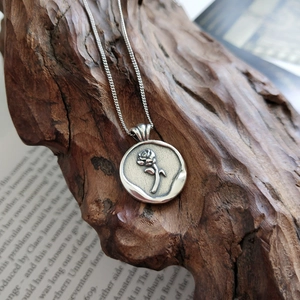 Vintage 925 sterling silver necklace with rose relief pendant on aged wood and book