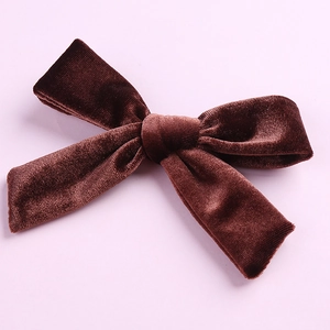 Detail of a dark brown velvet hair bow clip with soft texture on a purple background