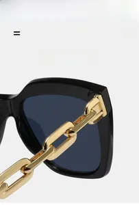 Detail of trendy square sunglasses featuring a bold gold chain temple and dark smoke lenses