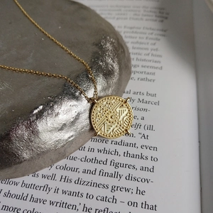 Detailed macro view of a gold coin pendant with geometric textures on a golden chain