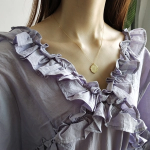 Golden round coin pendant necklace worn by a model in a lilac ruffled shirt