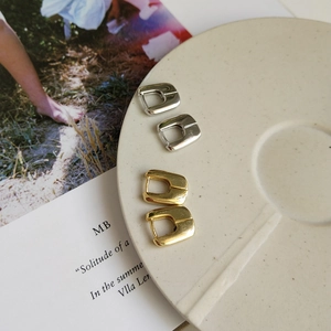 Detailed view of gold and silver geometric square earrings on a ceramic tray