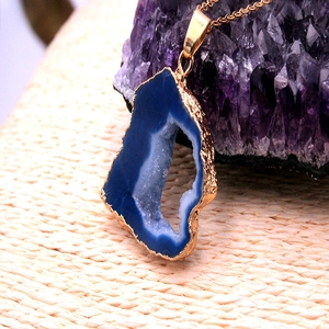 Primer plano del colgante de geoda de ágata azul chapado en oro sobre cristal morado