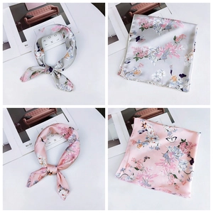 Detailed view of grey and pink floral silk square scarves displayed on a white table