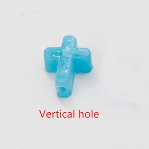 Detail of blue synthetic opal cross bead with visible vertical hole and fire luster