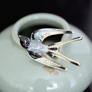 Close-up of enamel swallow brooch with blue wings and sparkling crystals on ceramic