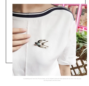 Detail of elegant swallow bird brooch with blue enamel inlay worn on white clothing