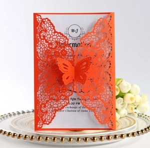 Detailed laser-cut butterfly lace wedding invitation in vibrant orange on a golden tray