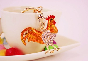 Close-up of golden metal rooster keychain with orange enamel and sparkling rhinestones
