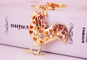 Close-up of golden metal rooster keychain with hollow heart patterns on a book background