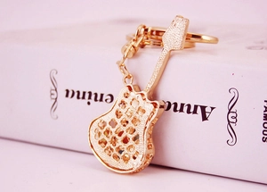 Close-up of golden hollow guitar keychain with rhinestones resting on a pink book
