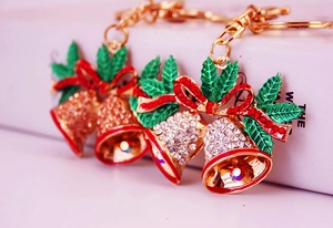 Close-up of golden Christmas bell keychain with rhinestones and green holly leaves
