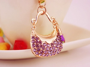 Close-up of golden handbag keychain with purple rhinestones and lipstick charm detail