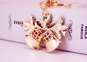 Close-up of golden Christmas bell keychain with green enamel leaves and polished finish