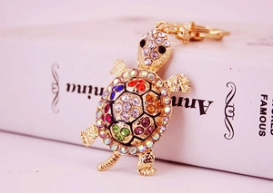 Detail shot of golden turtle keychain featuring colorful rhinestones on a prop book