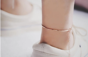 Close-up of a minimalist rose gold snake chain anklet worn on the ankle with casual shoes