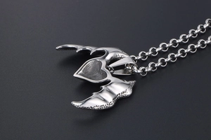 Detailed view of silver heart and wing pendant with metal chain on dark background