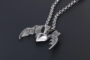 Detailed close-up of a silver metal heart pendant with bat wings on a round link chain