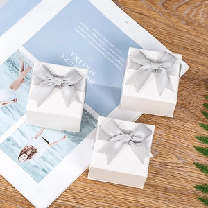 Three white square jewelry gift boxes with silver satin bows on a wooden surface