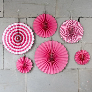 Set of 6 pink decorative paper fans with stripes and dots hanging on a stone wall
