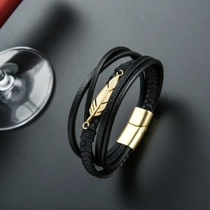 Detailed close-up of multi-layer black leather bracelet with golden feather charm and clasp