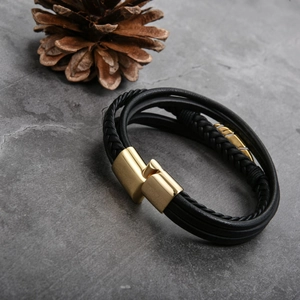 Detail of multi-layer black leather bracelet featuring a sleek golden magnetic clasp
