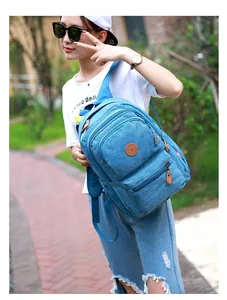 Outdoor shot of a blue canvas backpack featuring multiple zipper pockets and leather logo