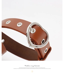 Macro detail of brown leather belt featuring silver heart buckle and metal eyelets