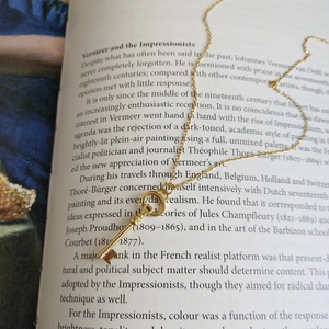 Close-up of golden key pendant necklace resting on an open art book page
