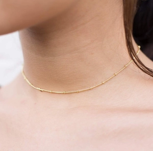 Dettaglio macro della collana a catena con sfere dorate indossata per un look minimalista