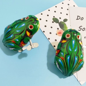 Detailed view of two vintage green clockwork tin frogs with wind-up keys on a blue background