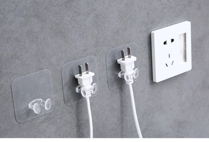Close-up of three transparent adhesive wall hooks for organizing power cord plugs on tile