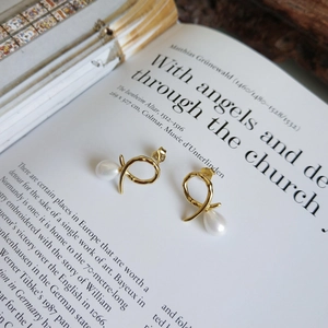Close-up of golden twist earrings with teardrop pearls on a vintage book background