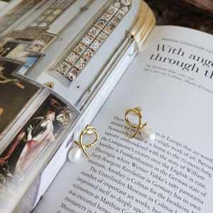 Artistic shot of gold ribbon knot pearl earrings placed on an open book background