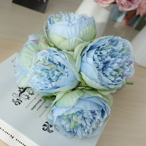 Close-up of light blue silk peony bouquet with multi-layered petals on a book