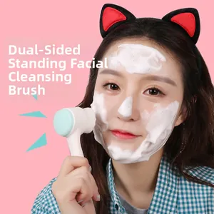 Dual-sided facial cleansing brush with soft bristles and silicone standing on a pink background