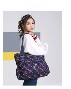Detailed side view of a large navy blue plaid nylon tote bag held by a model in casual attire