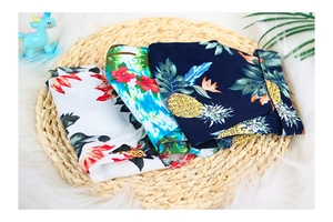 Detail of tropical pineapple and floral print shirts for dogs on a woven straw mat