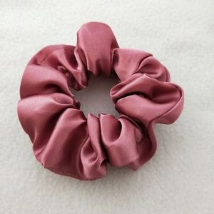 Detail of soft dusty pink satin scrunchie with glossy pleated texture on a fabric surface