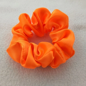 Close-up of bright orange satin scrunchie with smooth silk texture on white fur background