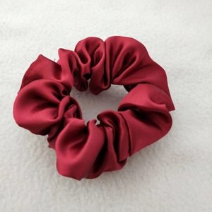 Close-up of a premium red satin silk scrunchie on soft white plush fabric background